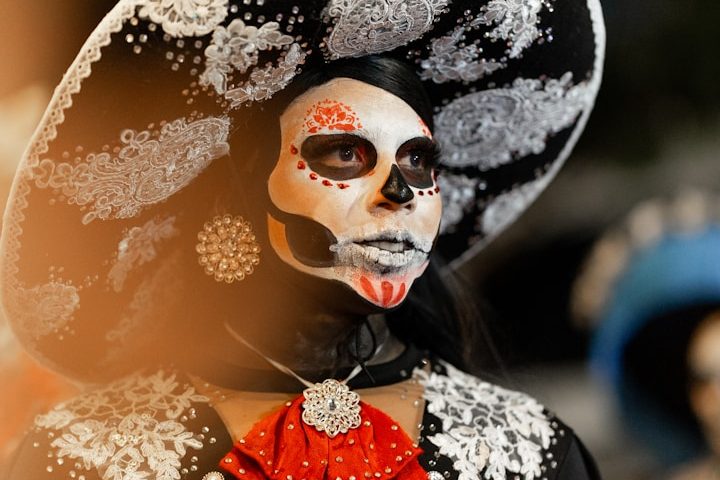 Woman in a decorative skull mask and wide-brimmed hat, adorned with flowers and jewellery.